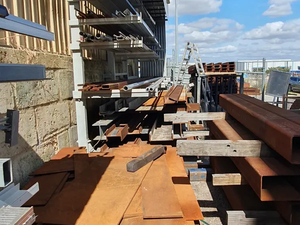 Steel plate stacked on the ground beside racks of long aluminium and steel lengths